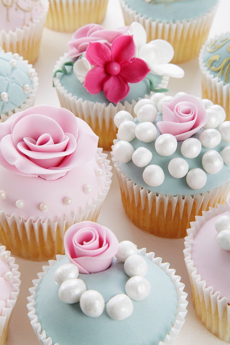 Verschiedene festliche Cupcakes mit Zuckerrosen und Perlen
