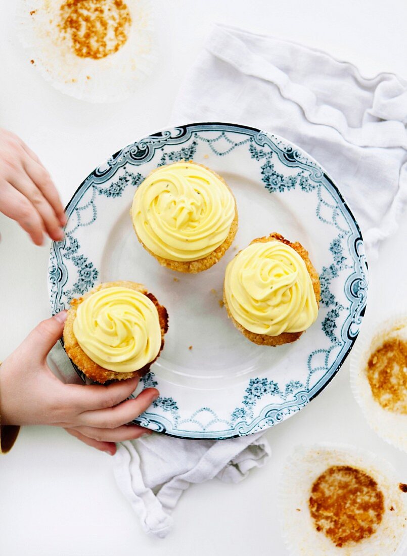 Hands reaching towards cupcakes which are on a plate