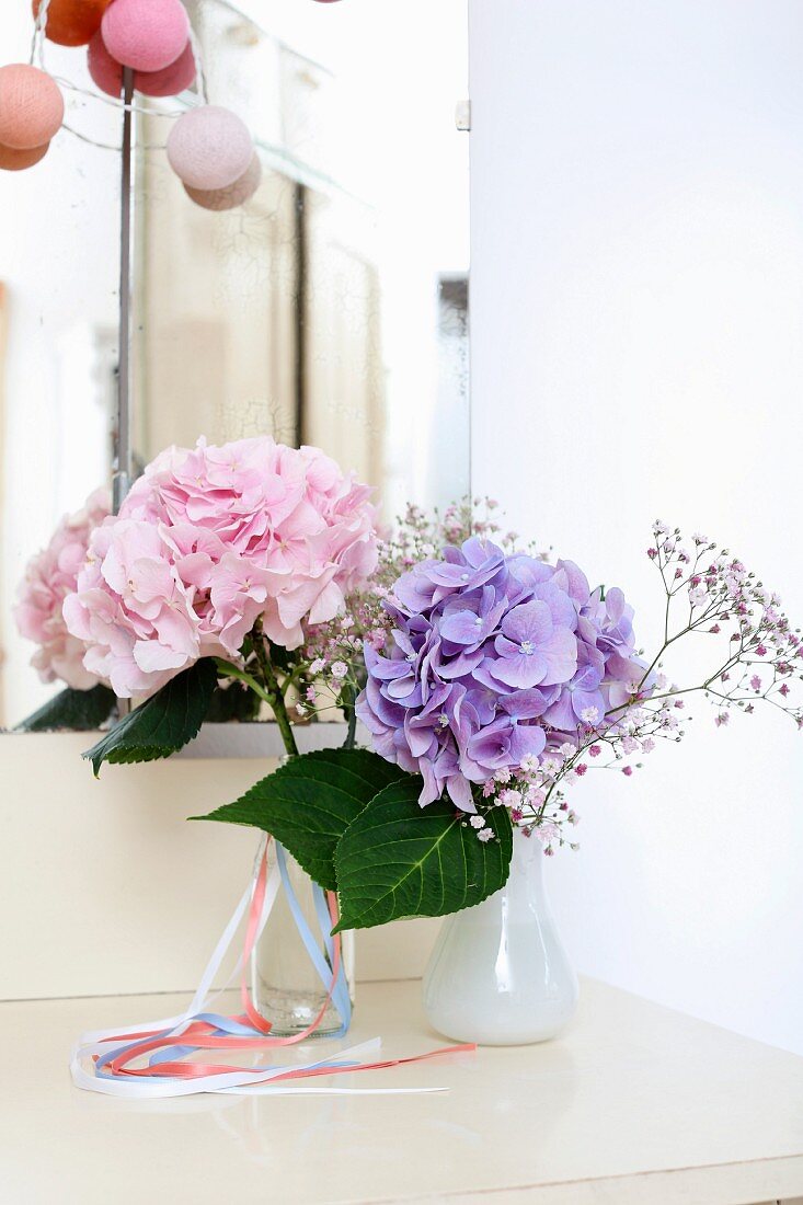 Small vases of pink and blue hydrangeas in front of mirror