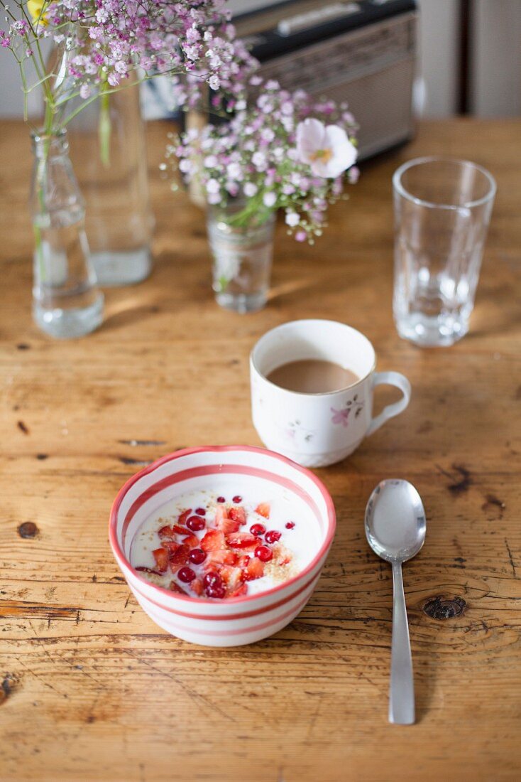 A bowl of muesli with yoghurt and a cup of coffee on a wooden table