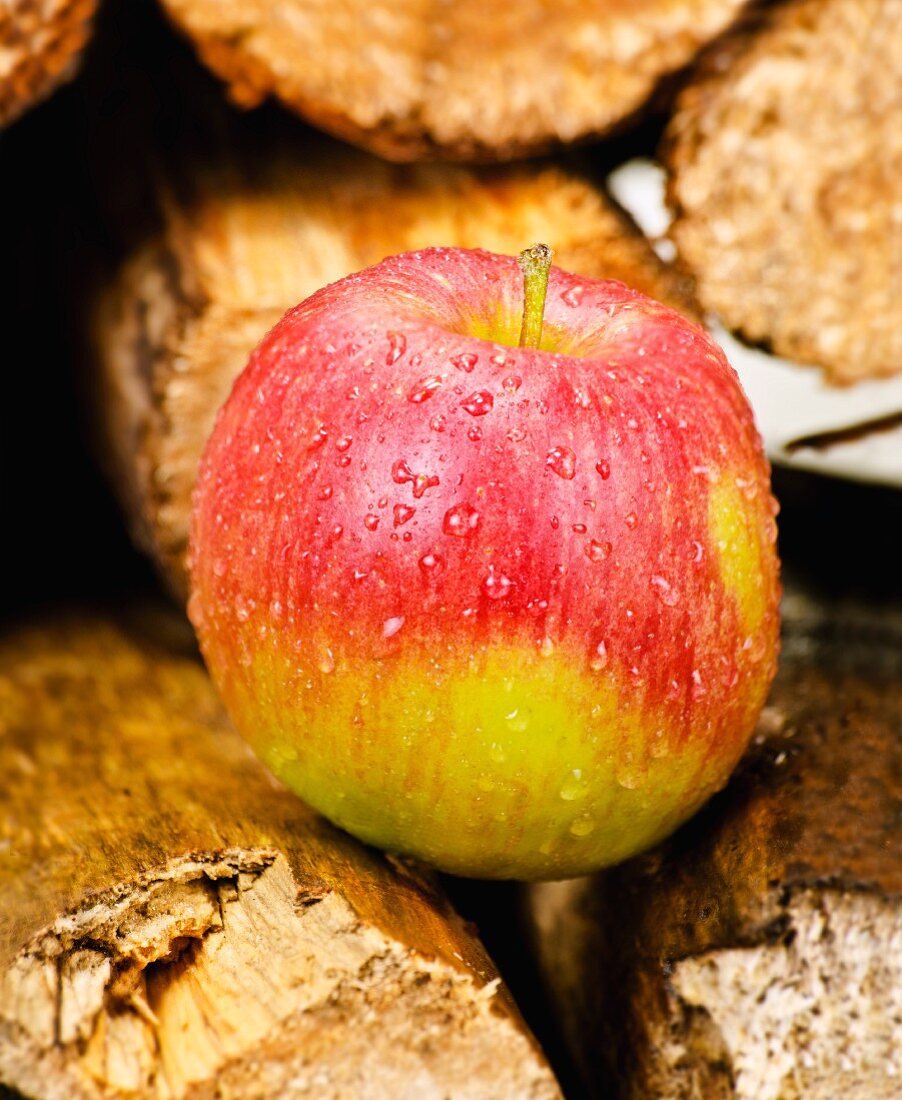 One red apple with droplets of water on a stack of wood