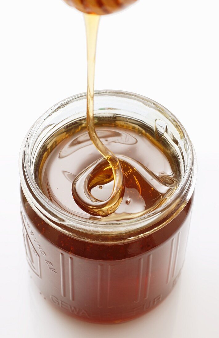 Honey trickling from a honey dipper into a jar