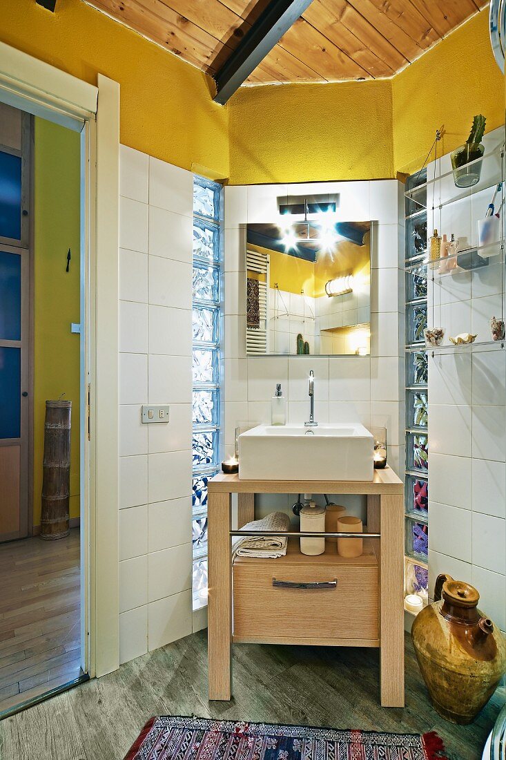 Modern wooden washstand with countertop basin against white-tiled wall in corner of bathroom