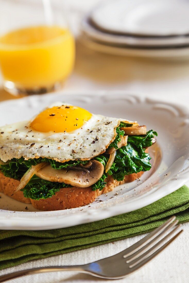 Kale and Mushrooms Topped with a Fried Egg on a Piece of Toast; Glass of Orange Juice