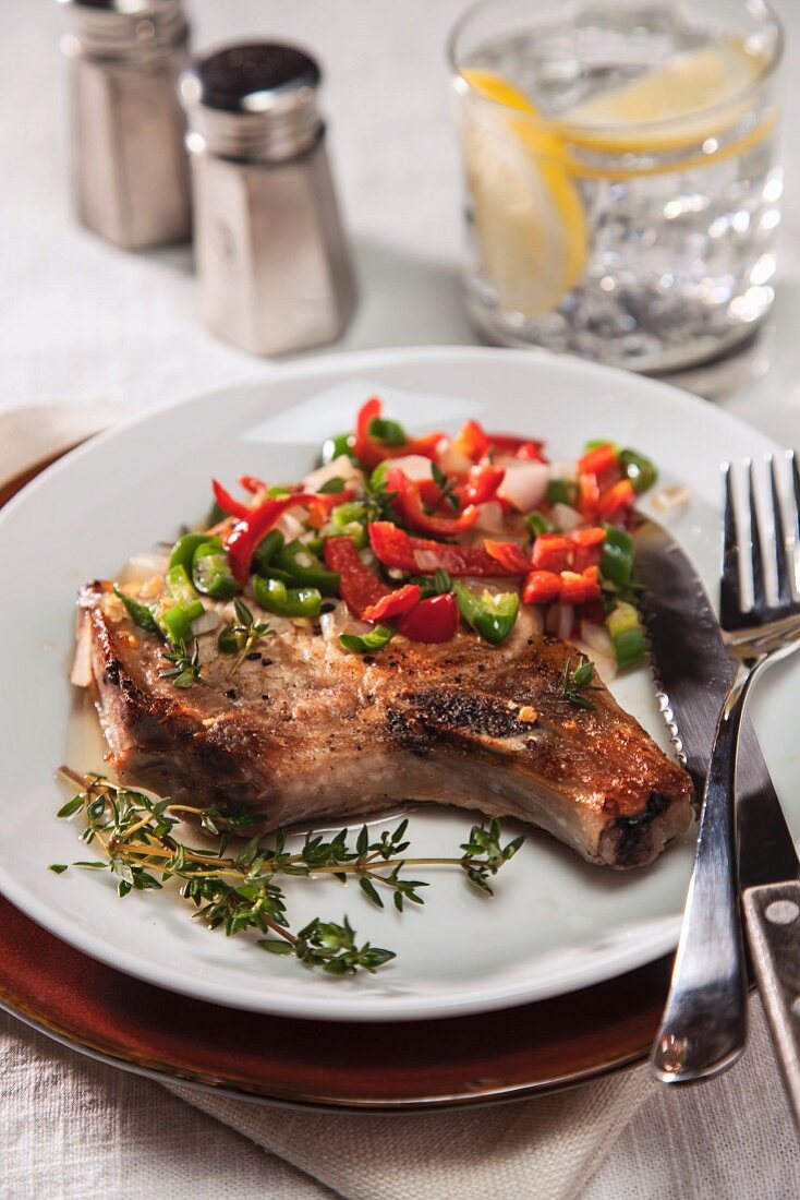 Grilled Bone-In Pork Chop with Sauteed Onions and red and Green Chili Peppers on a White Plate