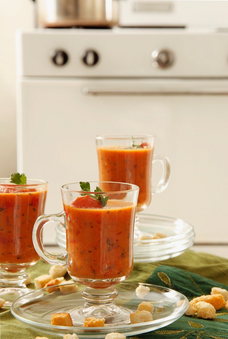 Three Tall Glass Mugs of Creamy Tomato Basil Soup; Croutons