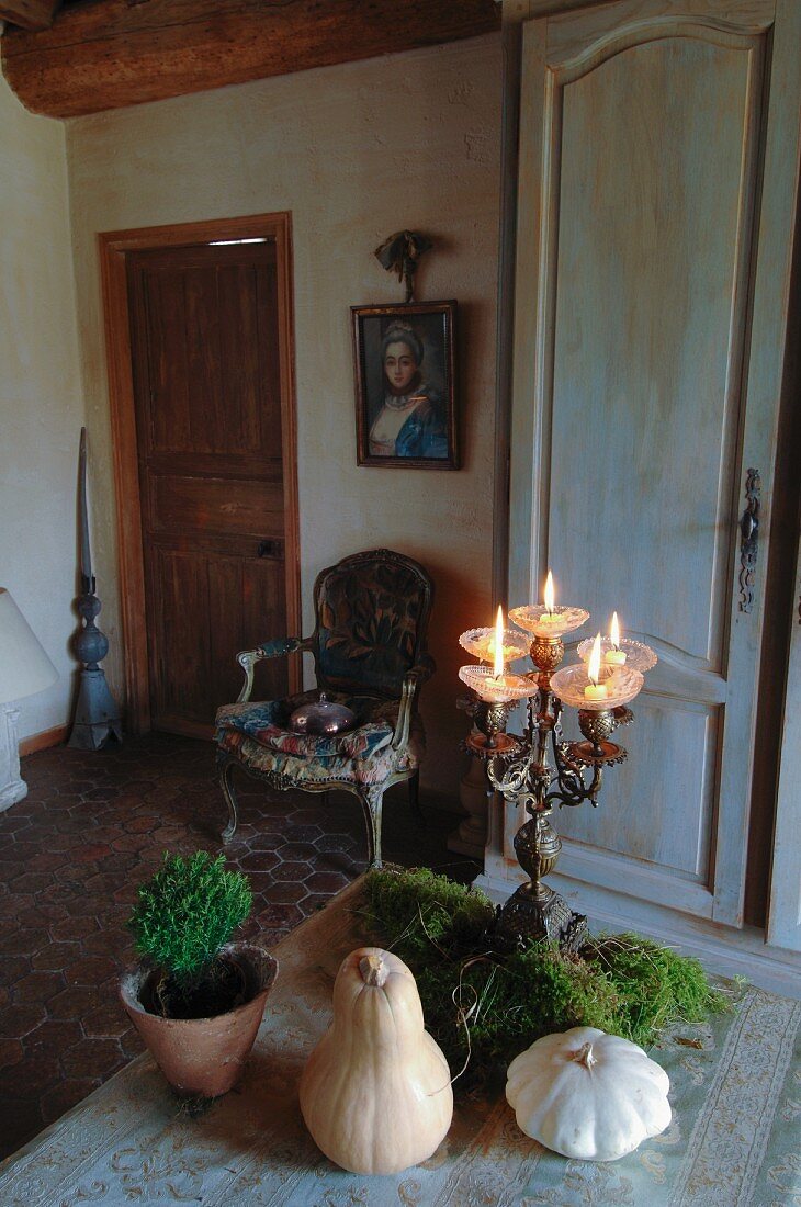 Antique candlestick and small, ceramic pumpkins on table; old portrait of woman above Rococo chair in background