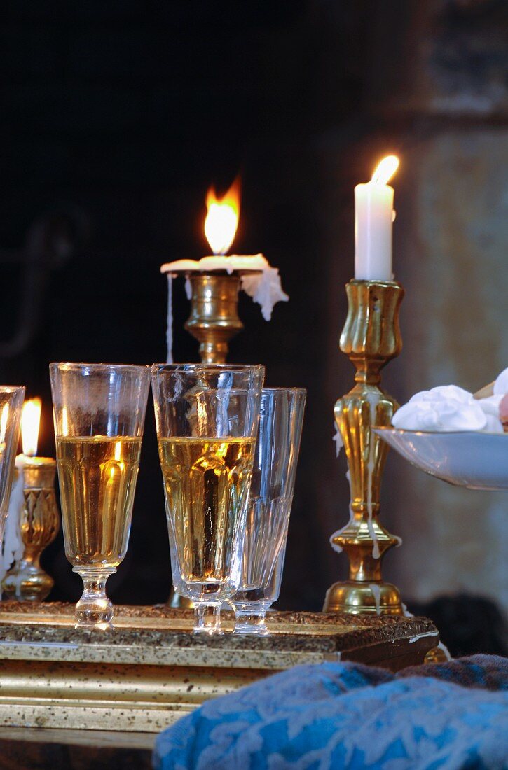 Gefüllte Sektgläser auf Tablett vor Messing-Kerzenständern mit brennenden Kerzen