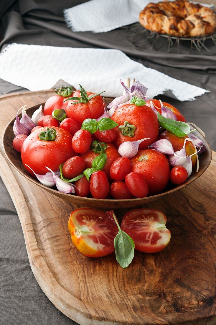 Verschiedene Tomaten und Knoblauch in Olivenholz-Schüssel auf Olivenholz-Brett