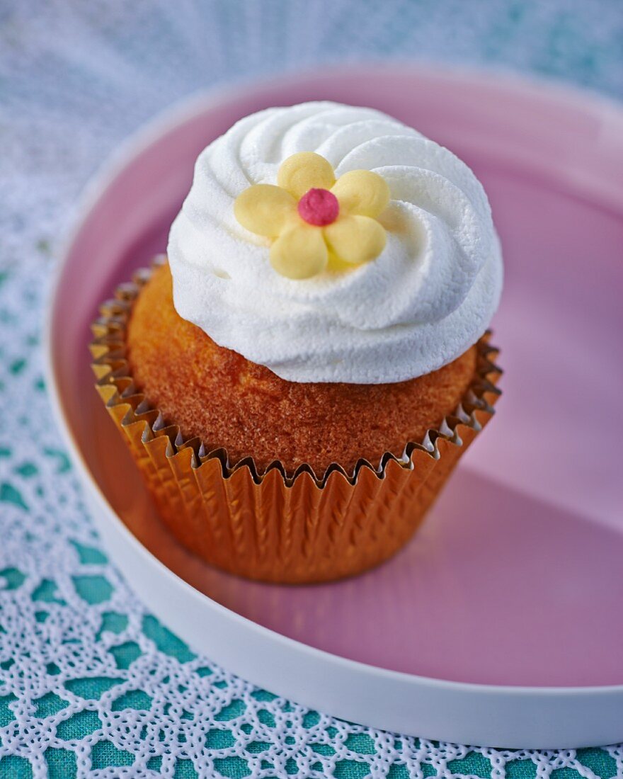 A cupcake topped with icing and a decorative flower