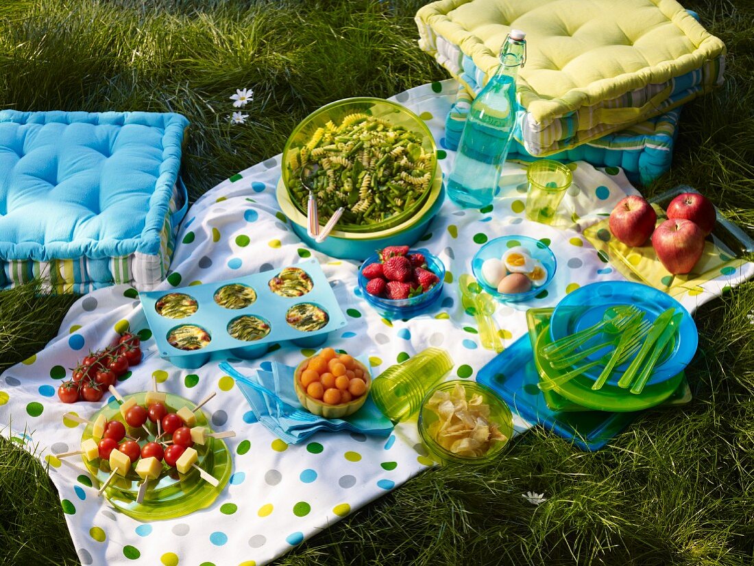 A picnic with a brightly coloured picnic blanket and floor cushions