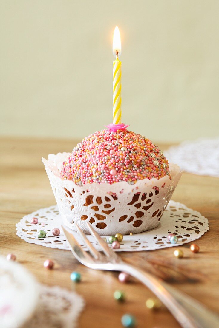 A cupcake decorated with colourful sugar sprinkles and a candle