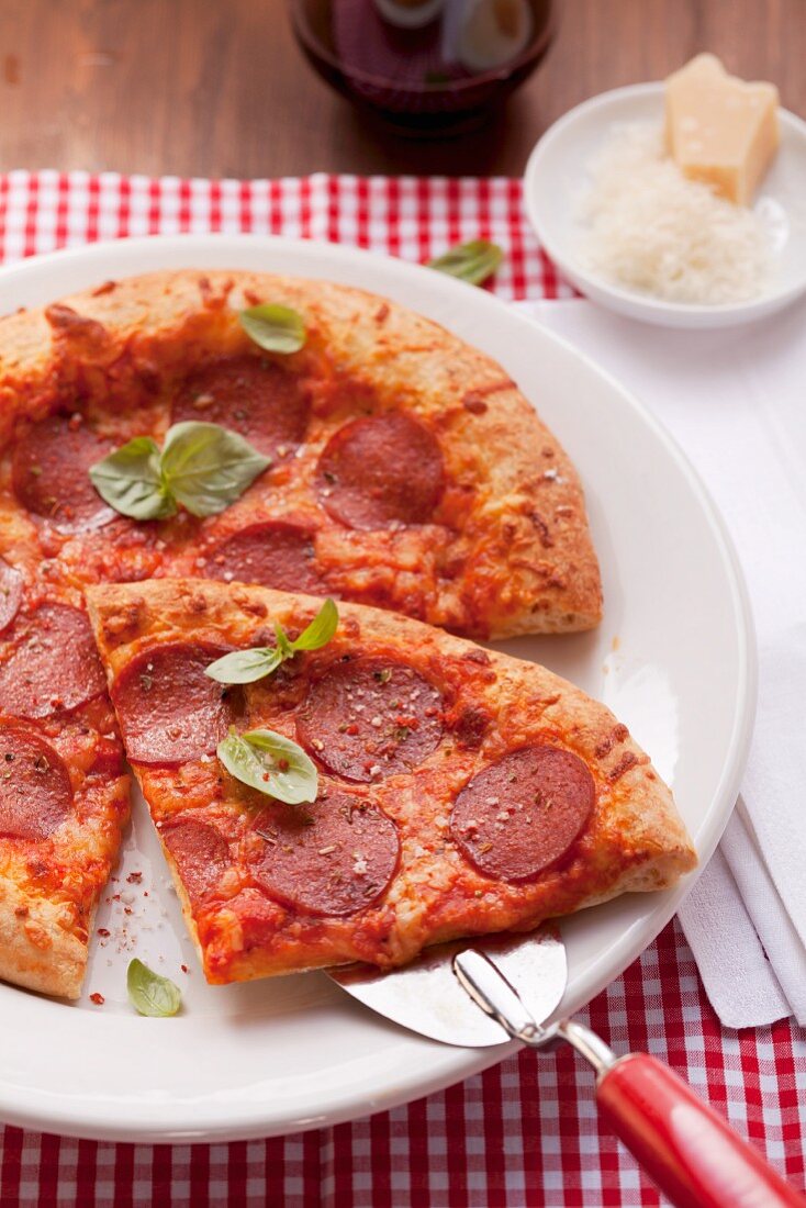 Pizza with salami and basil; one slice of the pizza is on a pizza shovel