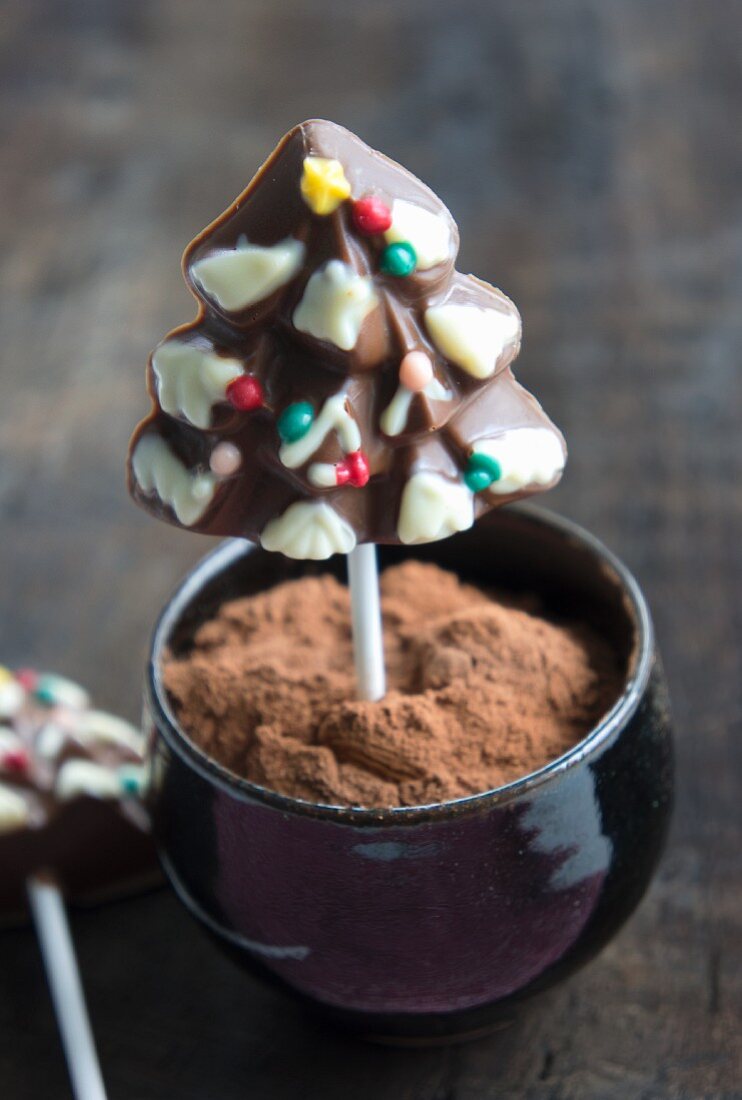 A chocolate Christmas tree on a stick in a bowl of cocoa powder