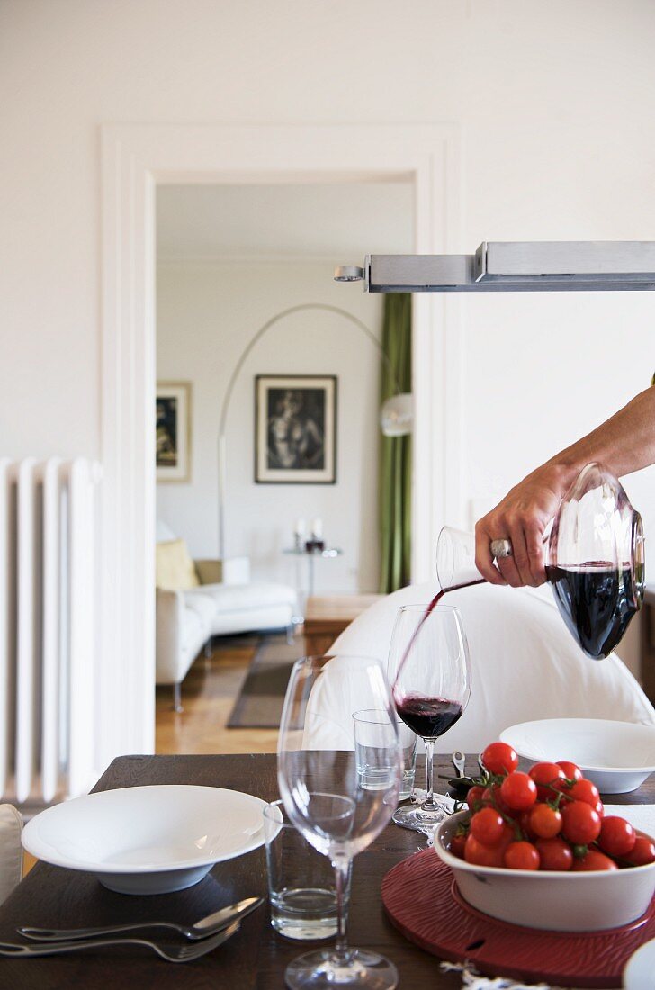 Frau giesst Rotwein in ein Glas am gedeckten Tisch