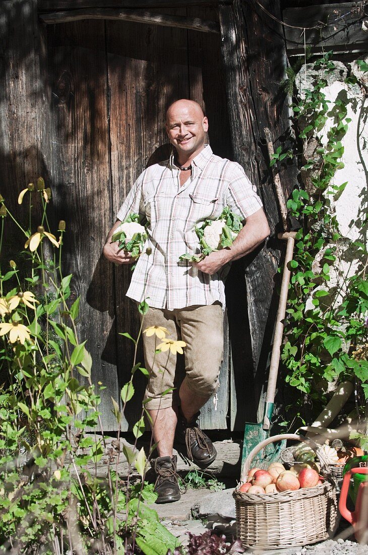 Mann hält Gemüse vor einer Holzscheune