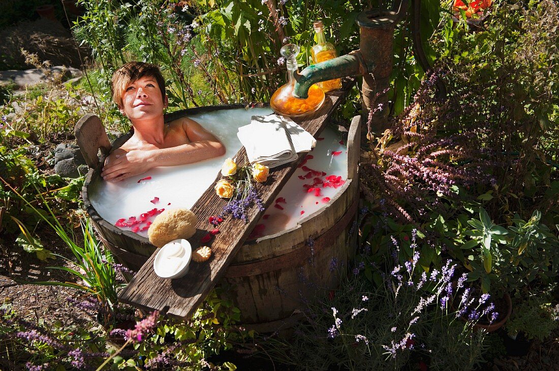 Frau nimmt ein Milchbad in einem Holzbottich im Garten