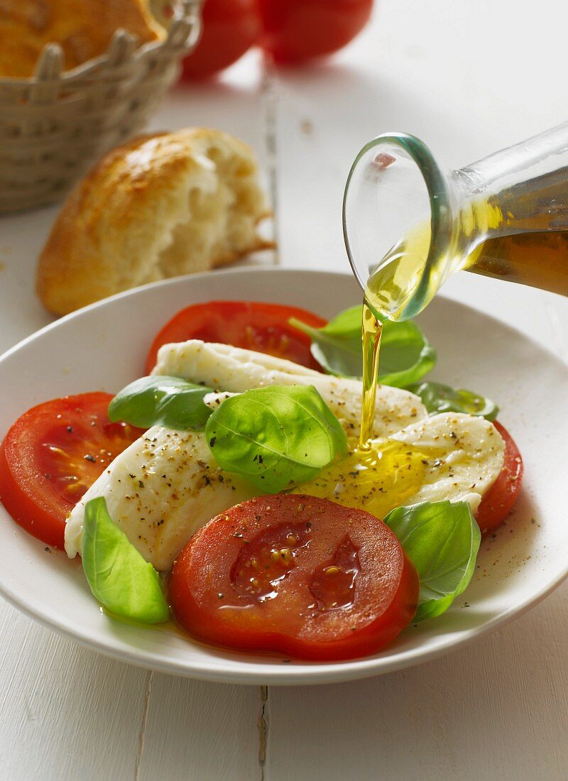 Tomatoes with mozzarella and basil being drizzled with olive oil