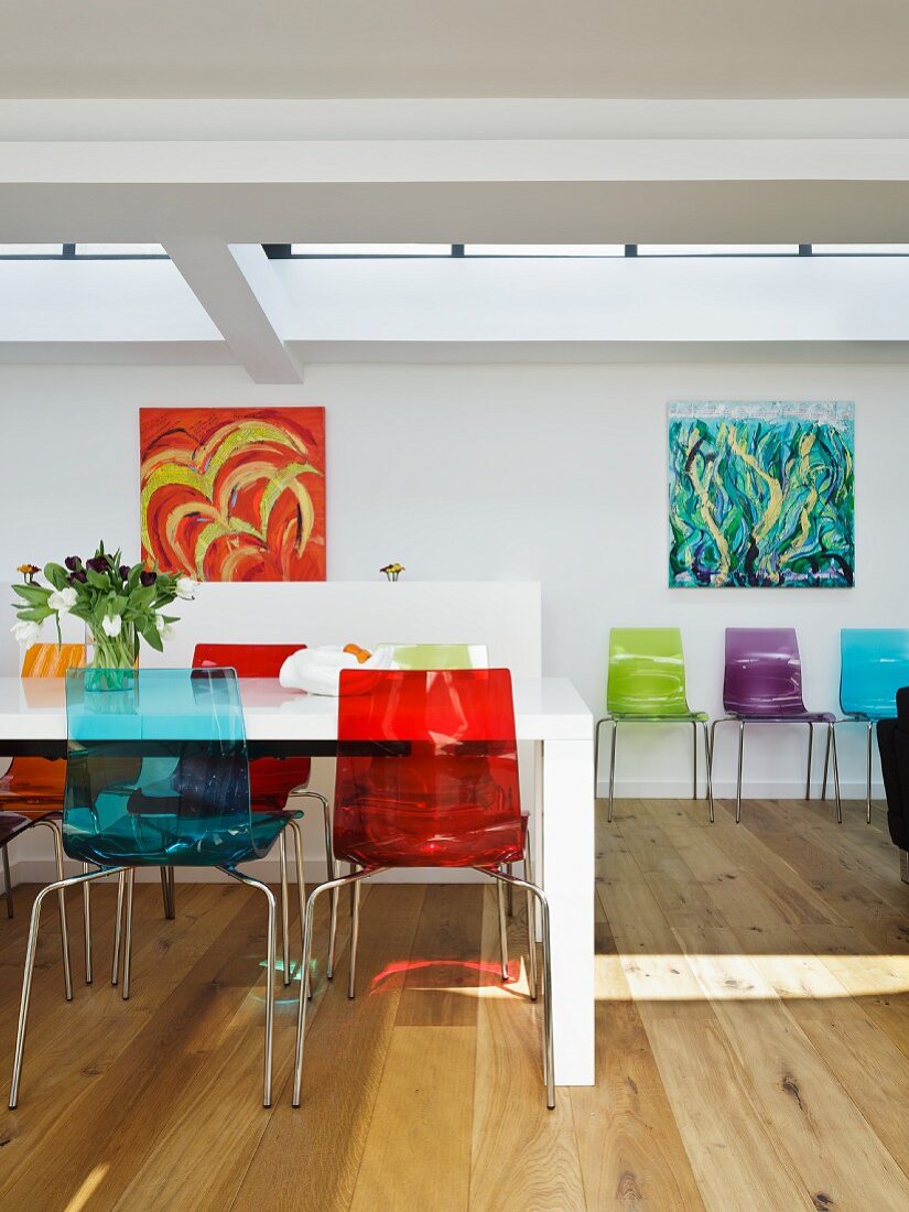 Farbige Kunststoff Stühle an weißem Esstisch gegenüber Wand mit modernen Bildern