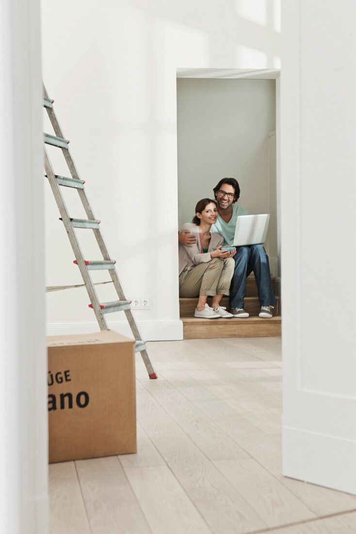 Couple sitting in doorway of new apartment with stepladder and packing case