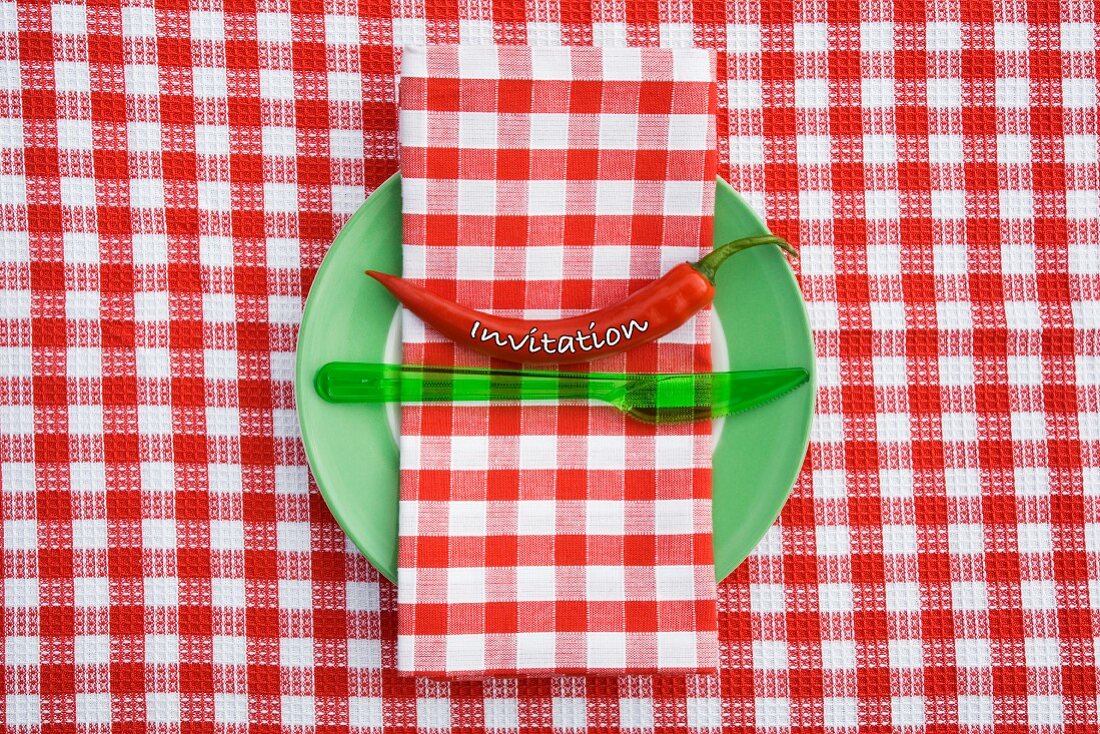 A place setting for an invitation, with a chilli pepper and gingham napkin