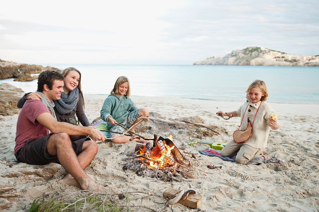Friends cooking sausages over a campfire on the beach