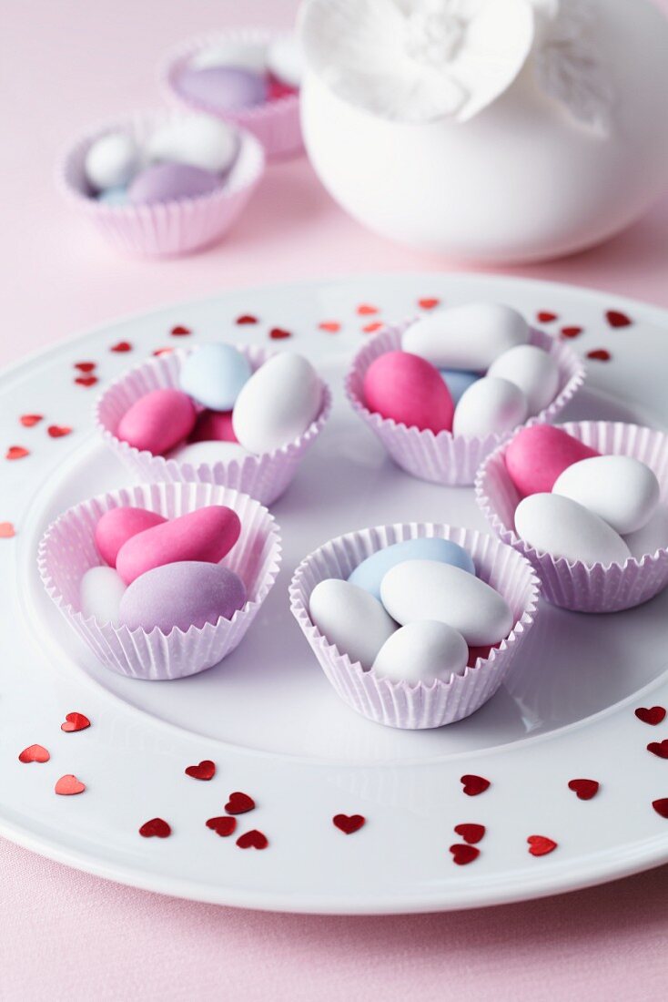 Sugared almonds in muffin cases on a plate scattered with hearts for a wedding