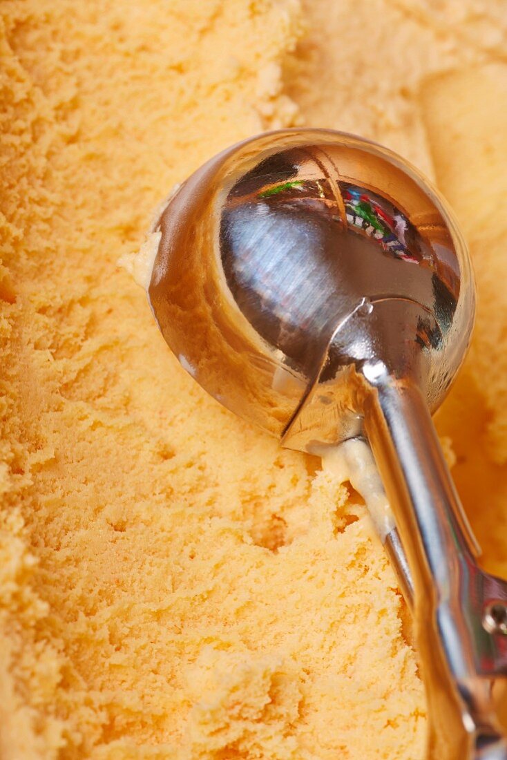 An ice-cream scoop creating a scoop of mango ice cream