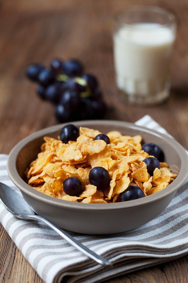 Cornflakes with red grapes, with a glass of milk in the background