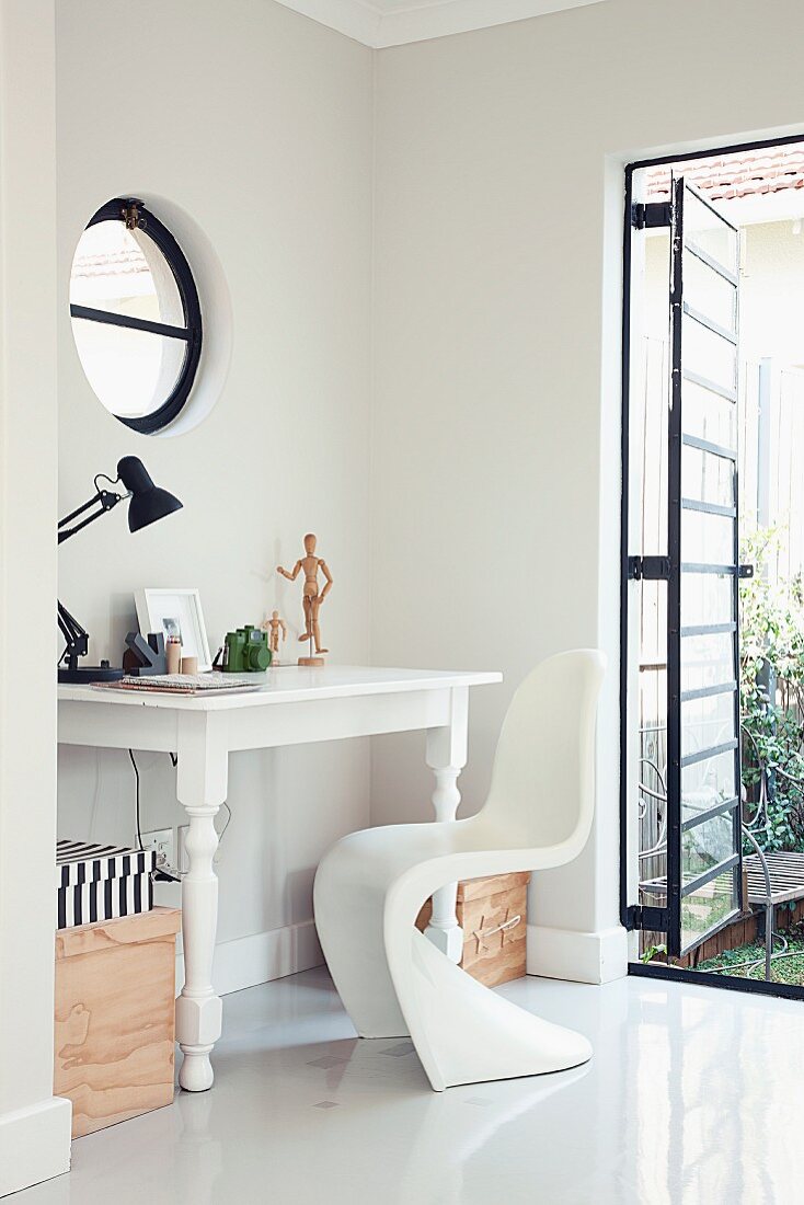 White, antique table and Panton chair in corner of room with metal-framed, industrial-style French window