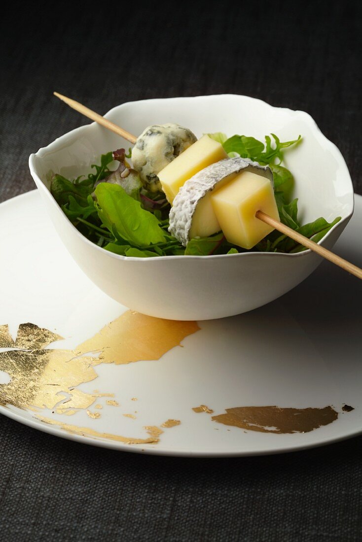 A cheese skewer on a bowl of salad leaves