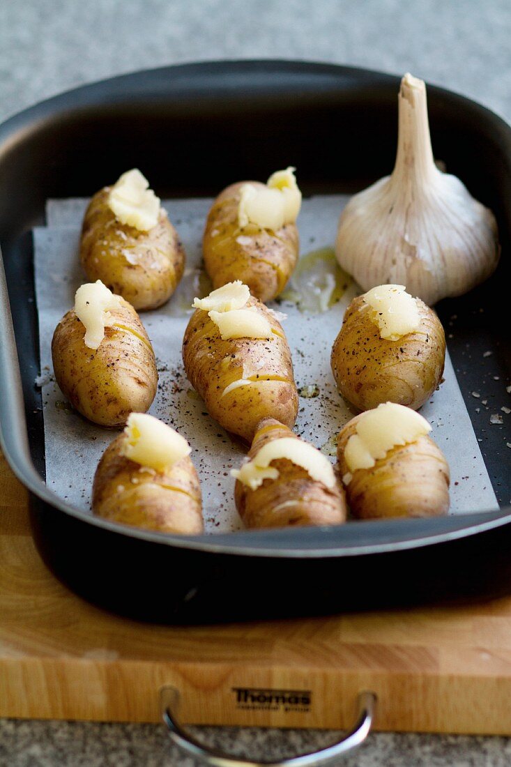 Raw Hasselback potatoes in a roasting tin, seasoned with salt, pepper and garlic butter