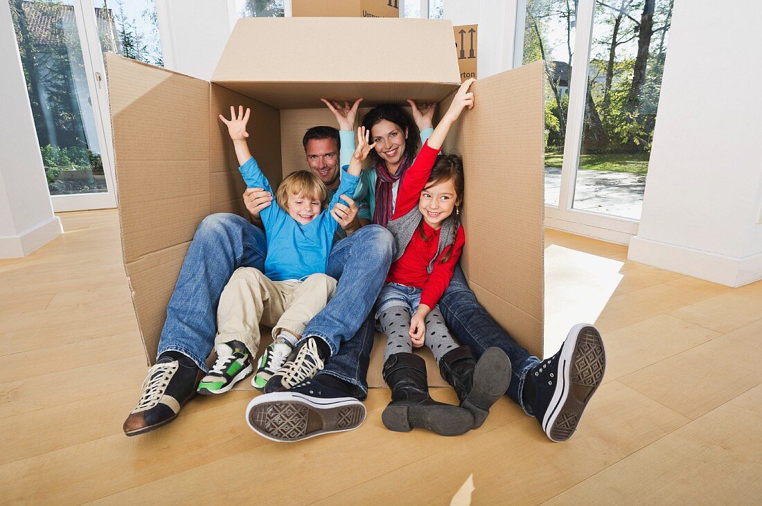 Family sitting in large packing case in empty living room