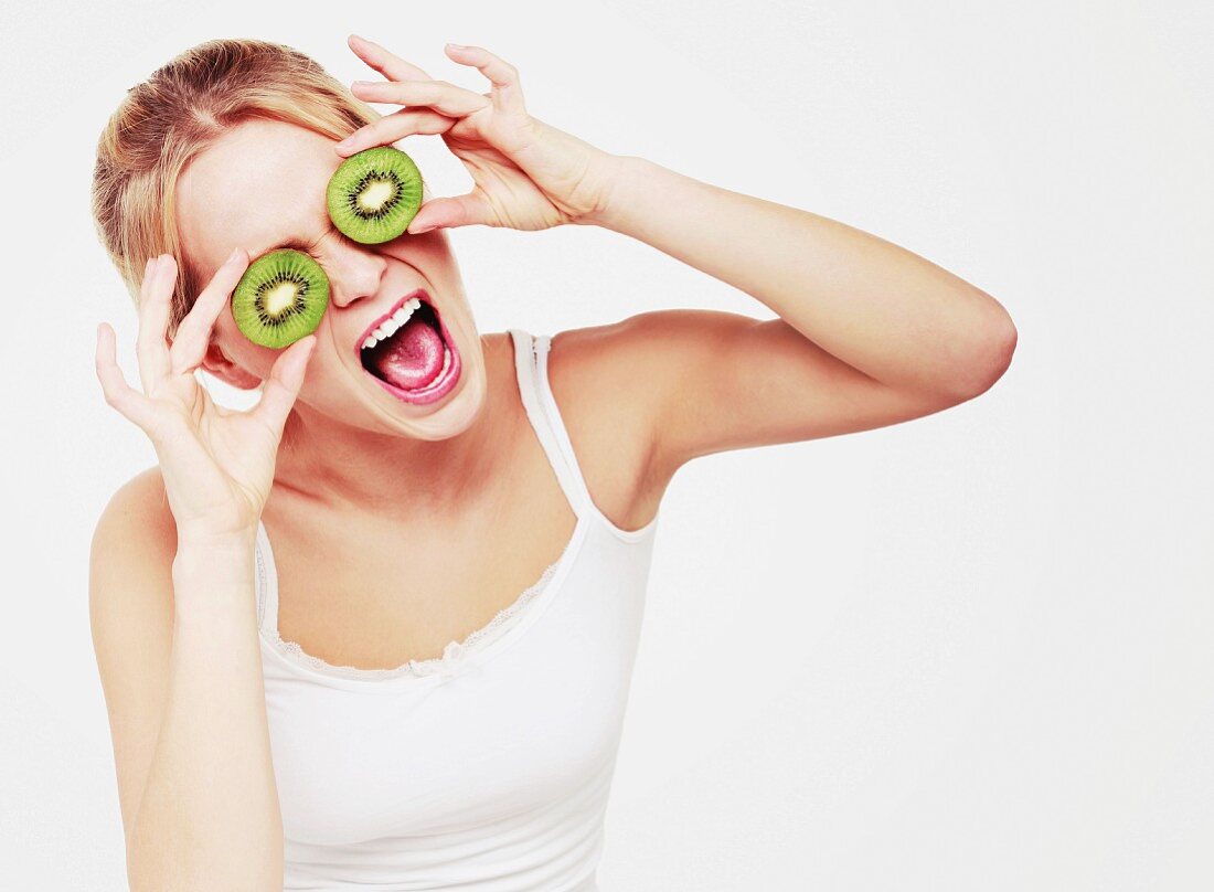 A woman holding kiwi slices in front of her eyes