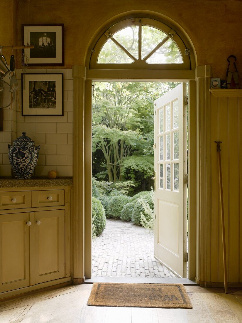 View into garden through wood and glass door opened outwards; stylish country house kitchen in soft, Shaker beige