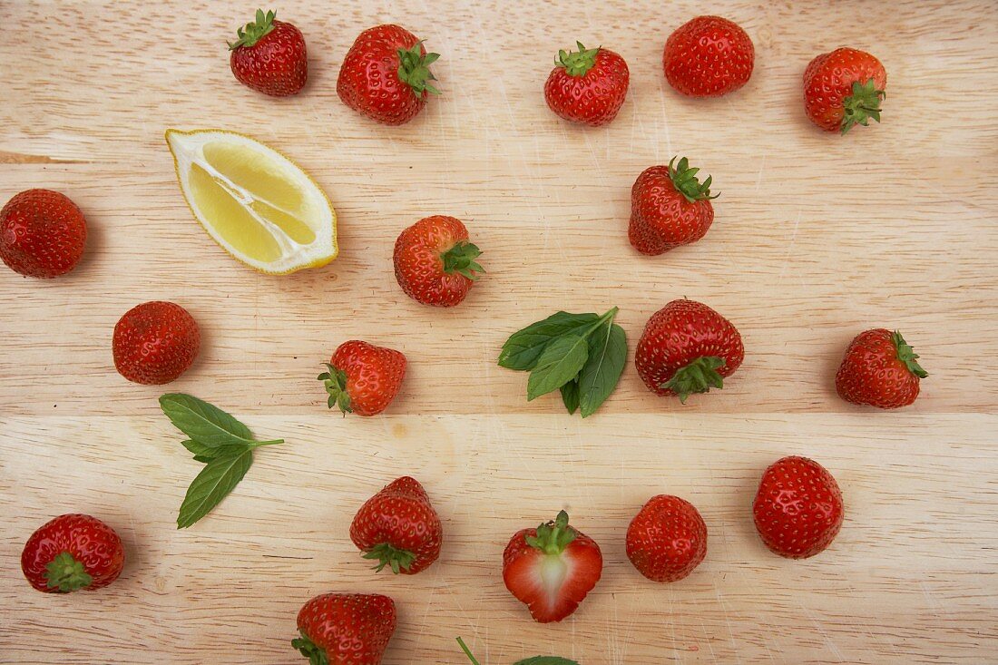 Fresh strawberries, mint leaves and a wedge of lemon on a wooden board