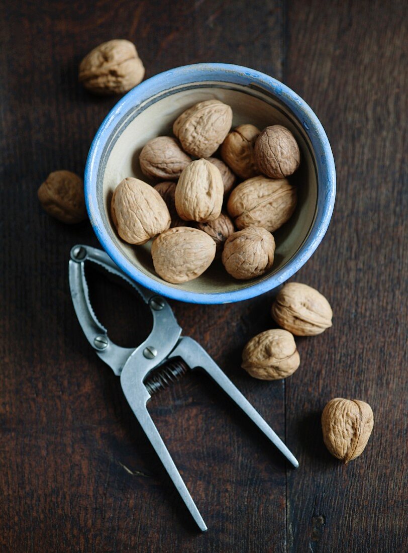 Walnuts in a bowl and a nutcracker on a wooden surface