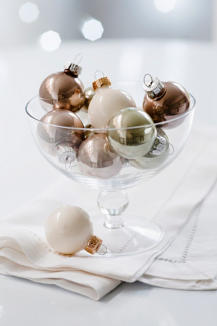 White, gold and silver Christmas tree baubles in a glass dish