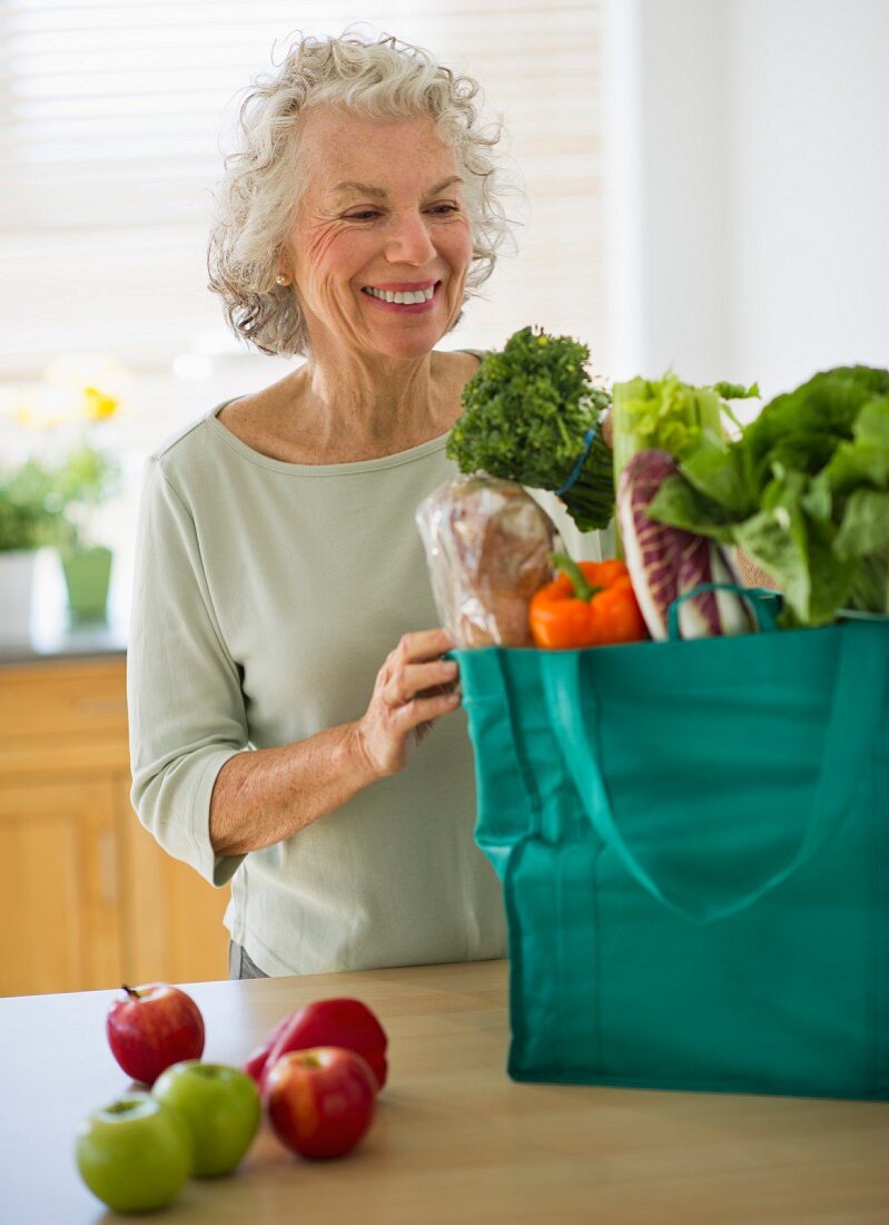USA, New Jersey, Jersey City, Senior woman with grocery bag in kitchen