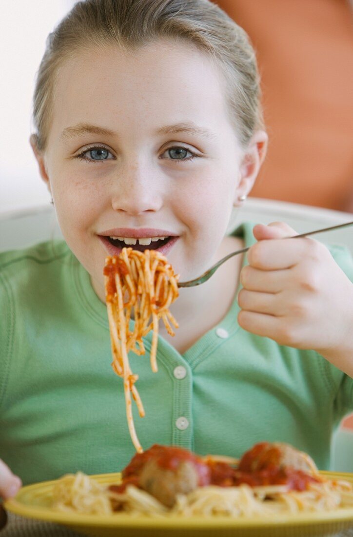 Mädchen isst Spaghetti mit Fleischbällchen und Tomatensauce