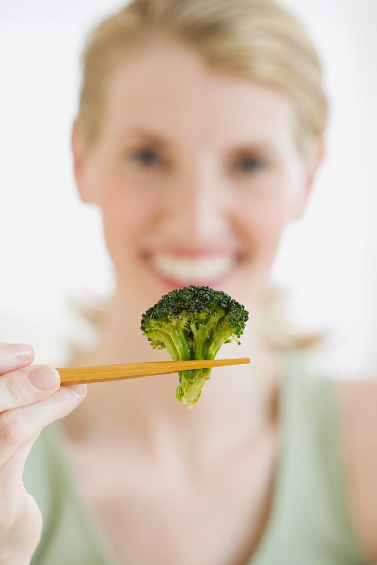 Woman holding broccoli in chopsticks