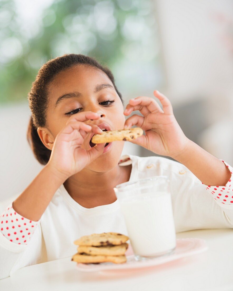 A girl eating a cookie with milk