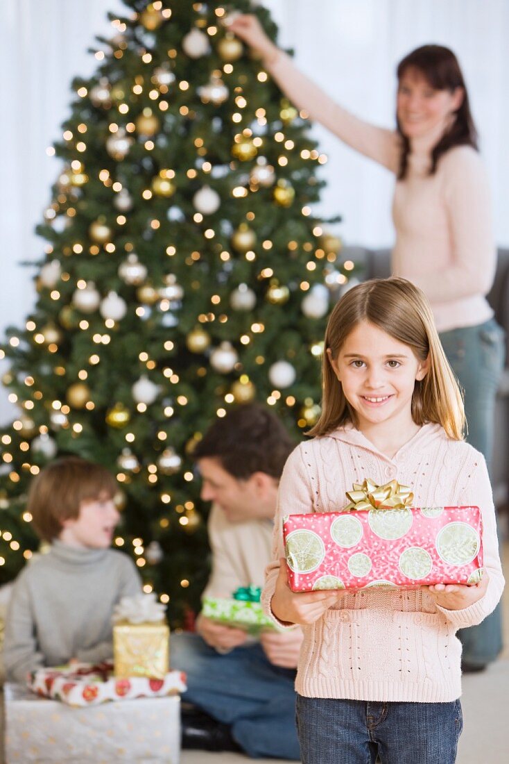 Mädchen hält Weihnachtsgeschenk vor Familie