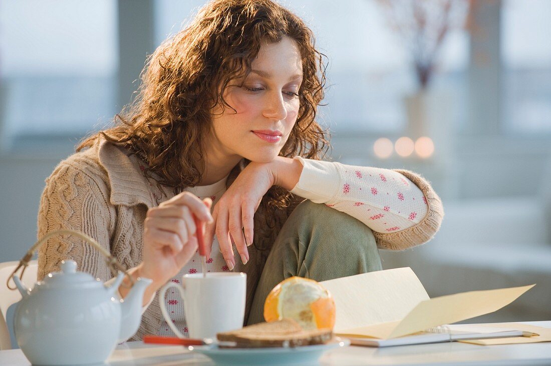 Woman reading letter and stirring tea