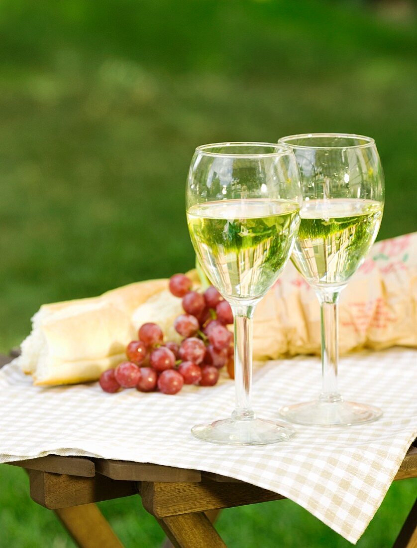 Weissweingläser, Weintrauben und Baguette auf Tisch im Freien