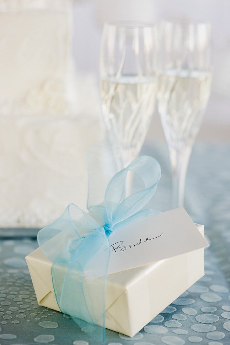 Hochzeitsgeschenk mit blauer Schleife und zwei Gläser Sekt