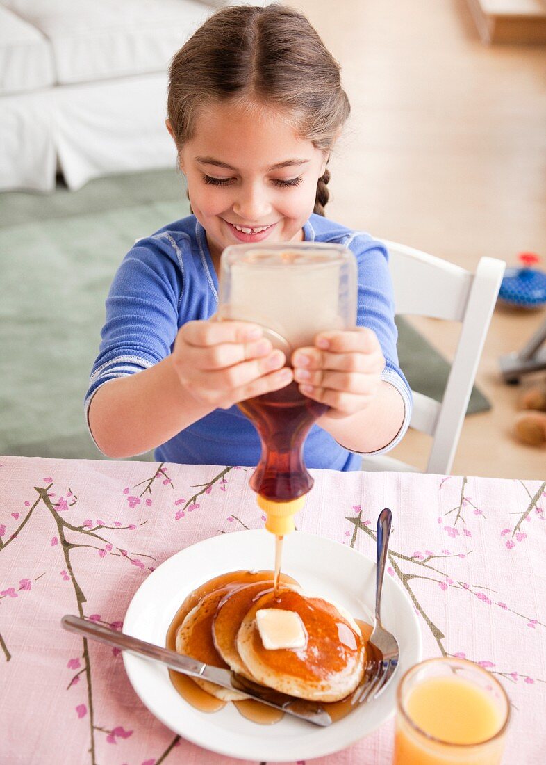 Mädchen gibt Ahornsirup auf Pancakes