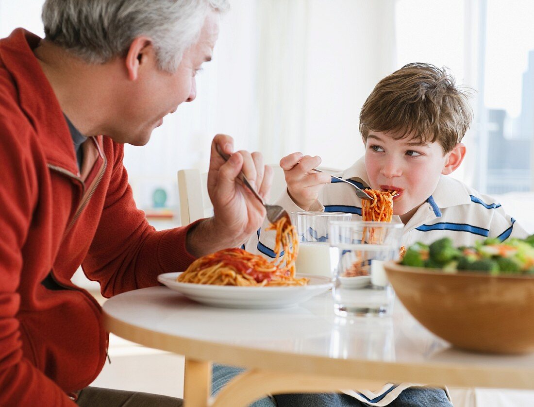 Vater und Sohn essen Spaghetti mit Tomatensauce