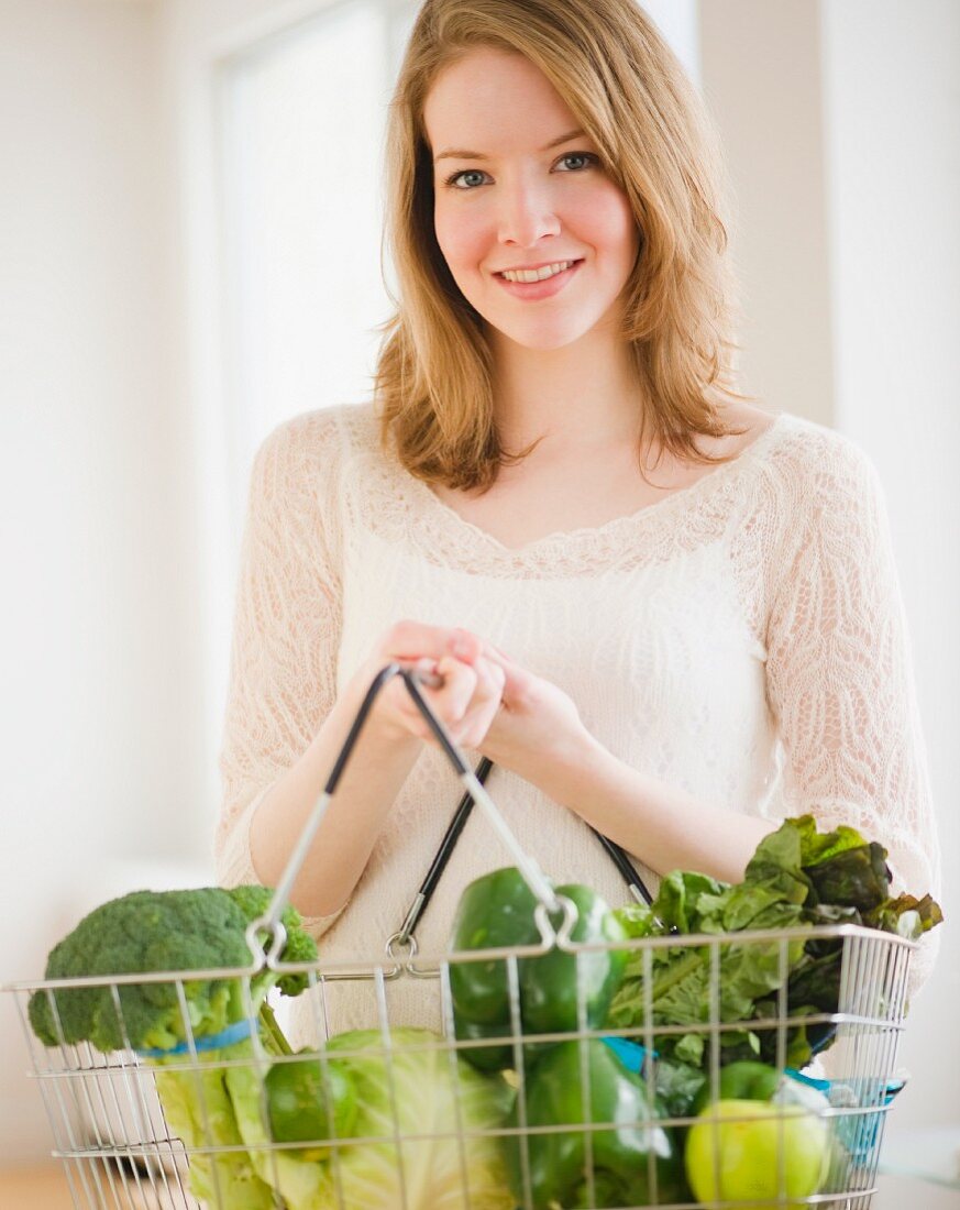 Junge Frau hält Einkaufskorb mit frischem Gemüse und Obst