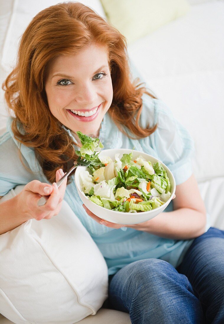 Frau isst auf Salat auf dem Sofa